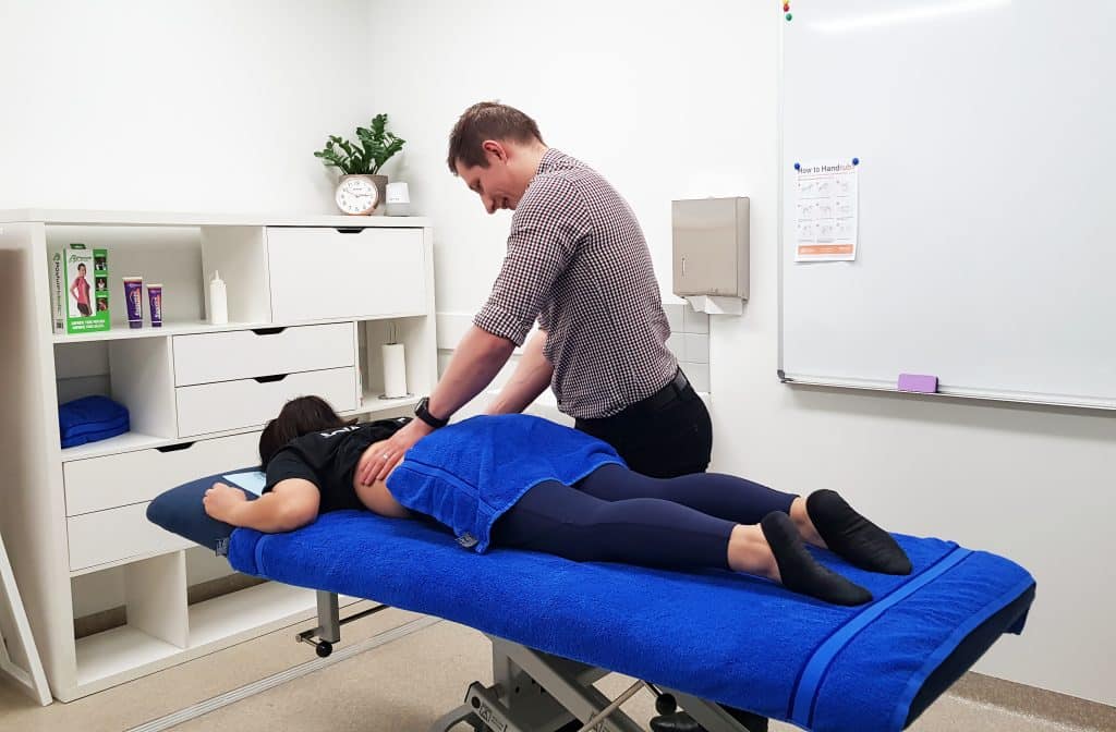 A photograph of a Physiotherapist treating a patients lower back on a treatment table.